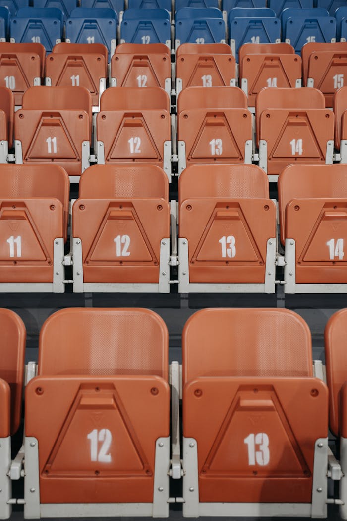 Close-up of orange and blue numbered stadium seats in vertical rows.